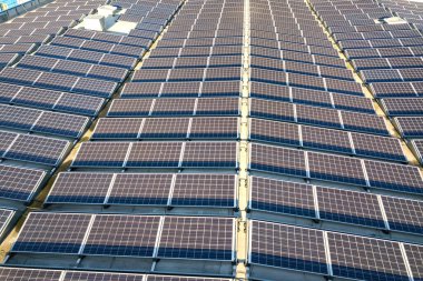 Sanayi binasının çatısına monte edilmiş birçok voltaik güneş panelinin hava görüntüsü.