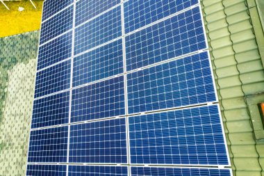 Çatıda mavi parlak güneş enerjili voltaik panelleri olan yeni, modern ev kulübesinin havadan görünüşü. Yenilenebilir ekolojik yeşil enerji üretim kavramı.