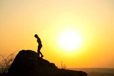 Gün batımında dağlarda büyük bir kayaya tırmanan bir kadın yürüyüşçünün silueti. Akşam vakti yüksek kayalıklarda gezen kadın turist. Turizm, seyahat ve sağlıklı yaşam tarzı konsepti.