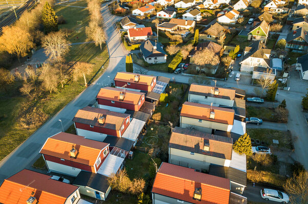 Вид с воздуха на жилые дома с красными крышами и улицы с припаркованными автомобилями в сельской местности. Тихие пригороды современного европейского города.