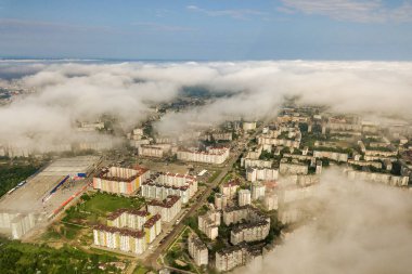 Yazın yeşil tarlalar arasında sıralı binalar ve kıvrımlı sokaklar olan bir kasaba ya da köyün üstündeki beyaz bulutların hava görüntüsü. Yukarıdan kırsal alan.