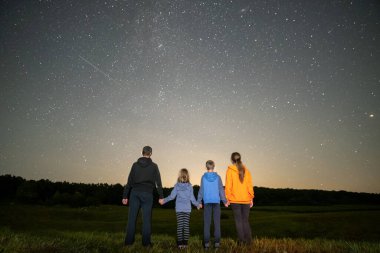Ebeveynler ve çocukları gece tarlasında durup bir sürü parlak yıldızla karanlık gökyüzünü izliyorlar..