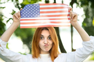 Yazlık parkta elinde ABD bayrağını tutan komik kızıl saçlı kadının portresi. Amerika 'nın bağımsızlık gününü kutlayan pozitif kız. Uluslararası Demokrasi Günü.