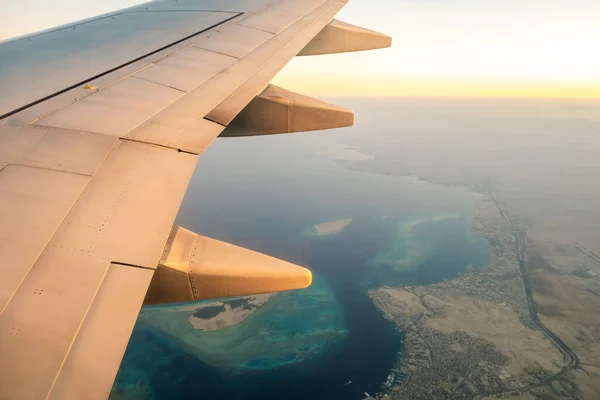 View from airplane on the aircraft white wing flying over ocean landscape in sunny morning. Air travel and transportation concept.