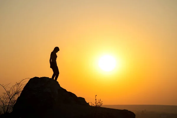 Silhouette of a woman hiker walking down a big stone at sunset in mountains. Female tourist on high rock in evening nature. Tourism, traveling and healthy lifestyle concept.