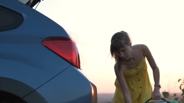 黄色のドレスの若い女性は車のトランクに緑のスーツケースを入れて 旅行と休暇のコンセプト — ストック動画