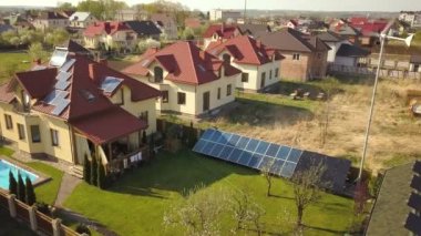 Yeşil çimlerle kaplı özel bir evin havadan görünüşü çatıda güneş panelleri, mavi su ve rüzgar türbini jeneratörlü yüzme havuzu..