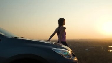 Genç bir kadın arabasının yanında gün batımını seyrediyor. Kız gezgin gece ufkuna bakarak araç kaputuna yaslanıyor..