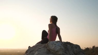 Genç, rahat bir kadın büyük bir taşın üzerinde oturmuş sıcak bir yaz gününün tadını çıkarıyor. Gün batımında meditasyon yapan ve dinlenen bir kız..