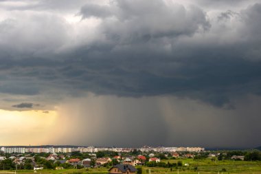 Kara fırtınalı bulutlarla kapkara bir manzara Yazın uzak kasaba binalarının üzerine sağanak yağmur yağıyor.