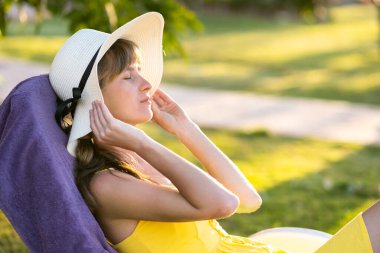 Genç bir kadın güneşli bir yaz gününde dışarıda dinleniyor. Mutlu bayan plaj sandalyesine uzanmış hayal kuruyor. Sakin, güzel, gülümseyen kız temiz havanın tadını çıkarıyor, kapalı gözlerle dinleniyor..