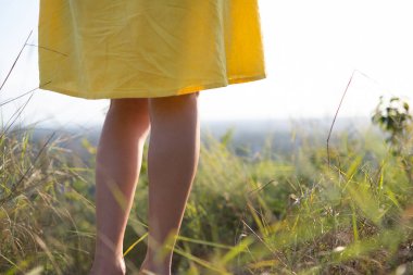 Sarı yazlık elbiseler içinde çimenli arazide duran genç kadın bacaklarını kapat..
