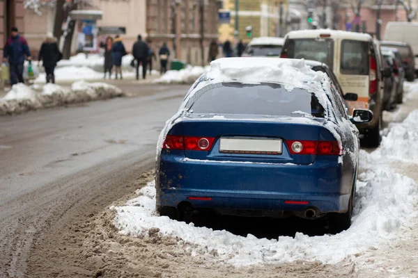 Cars parked on a side of city street covered with dirty snow in winter.