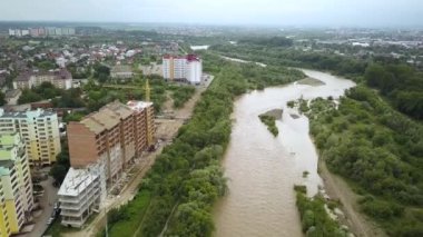 Çamurlu sarı suyla dolu geniş, kirli nehrin havadan görünüşü ilkbaharda sağanak yağış sırasında sel altında bir şehre akıyor..