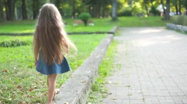 Güneşli bir günde yeşil bir yaz parkında açık havada yürüyen uzun saçlı güzel bir kızın arka görüntüsü..