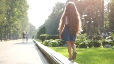 Güneşli bir günde yeşil bir yaz parkında açık havada yürüyen uzun saçlı güzel bir kızın arka görüntüsü..