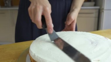 Kadın ellerine yakın beyaz krema ve bisküviyle tatlı pasta yapıyor..