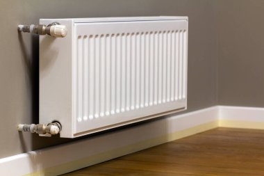 Beyaz metal ısıtma radyatörü bir odanın içindeki gri duvara monte edilmiş..