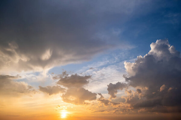 Dramatic yellow sunset landscape with puffy clouds lit by orange setting sun and blue sky.