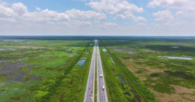 Açık güneşli bir günde Florida sulak arazisi boyunca düz bir otoyol boyunca devam eden araba ve kamyon hareketleri.
