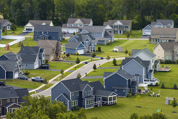 Aerial view of private residential houses in rural suburban sprawl area in Rochester, New York. Upscale suburban homes with large backyards and green grassy lawns in summer season.