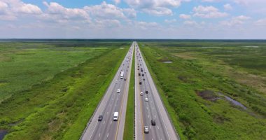 Florida otoyolu üzerindeki bulutsuz gökyüzü bataklık bitki örtüsü ve araba ve kamyonlarla dolu düz yol şeritleriyle dolu.