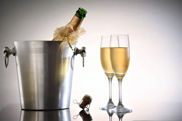 opened champagne bottle in cooler bucket with glasses on white background