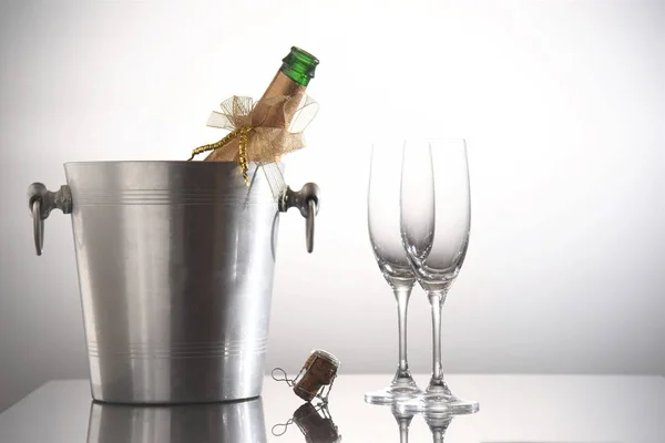 opened champagne bottle in cooler bucket with empty  glasses on white background