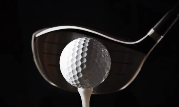 golf ball on tee with driver club head;studio shooting,high contrast lighting dark background
