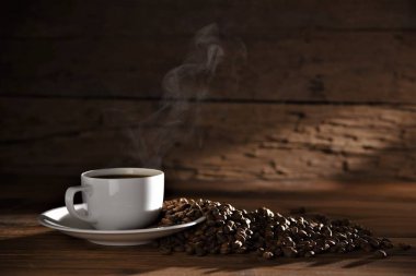 ahşap masa koyu arka plan üzerinde duman ve kahve çekirdekleri ile sıcak kahve fincanı