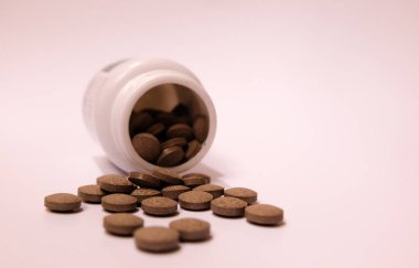 Beyaz kavanozdan çıkan kahverengi bitkisel haplar.