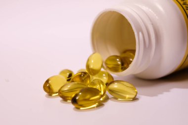 Beyaz kavanozdan çıkan sarı balık yağı kapsülleri.