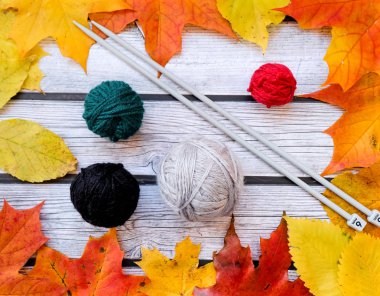 Örgü iğneleri ve yapraklarla çevrili iplik topları.