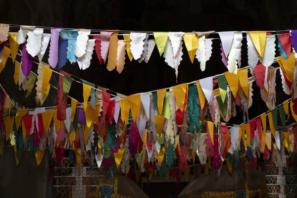 Flag banner decoration in buddhist temple. Triangle flags garland on dark background. Cambodian temple internal decor. Colorful flag ribbon. Buddhism festival decoration. Festive religious ritual