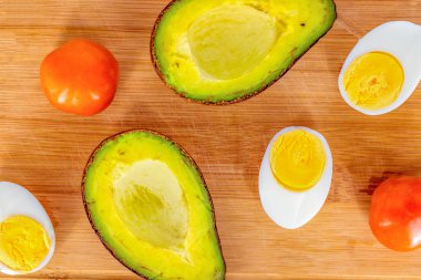 Avokado, domates ve yumurta ahşap tahta üzerinde. Taze doğal gıda. Organik sebze üstten görünüm. Avokado salatası malzemeler yemek. Yaz diyet tarifi. Lezzetli kahvaltı hazırlığı. Ahşap tahta düz yatıyordu