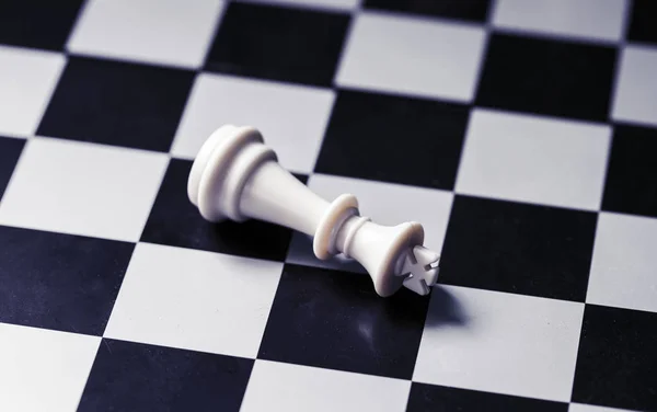 White king on chess board. King lost on checkered board. White king lies on chessboard. Mate situation in chess rules. Business advantage or strong leadership concept. Chess king closeup