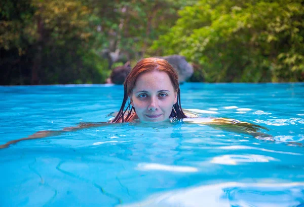 Swimming woman in open swimming pool. Girl in open swimming pool. Summer vacation experience photo. Tropical jungle hotel scene. Exotic holiday. Outdoor swimming pool. Girl in pool looking in camera
