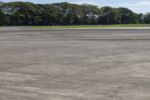 Yeşil alanıyla Havaalanı. Tropikal ülkede boş uçuş pisti. Yaz tatil seyahat hedef. Asfalt zemin üzerine yeşil ağaçlar alanıyla. Sarı işaretleri ile gri beton yolu. Güneşli Havaalanı