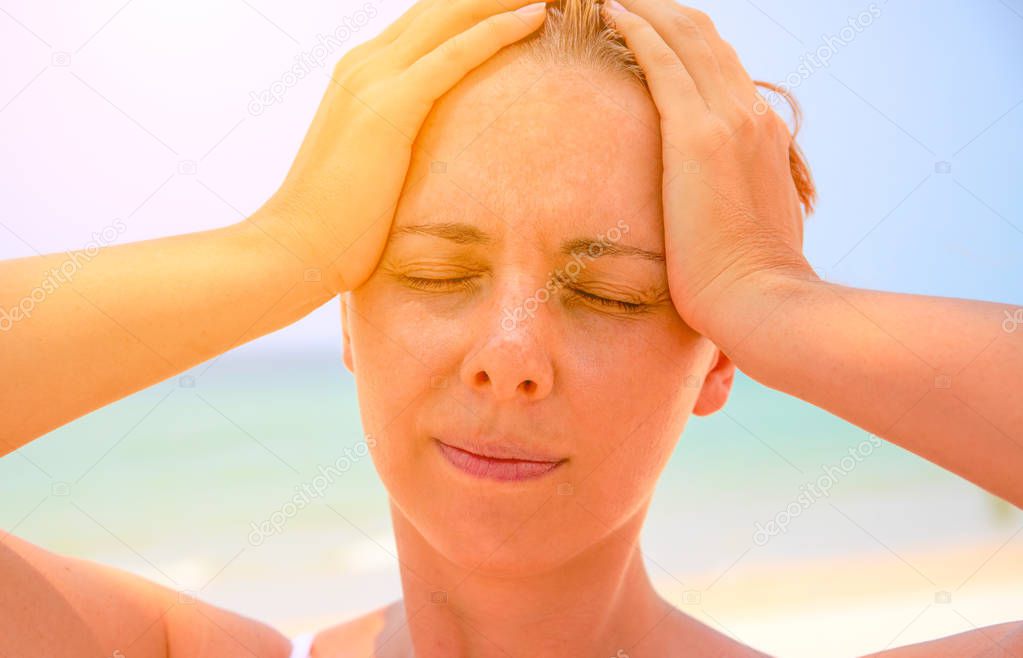 Young woman suffering with headache. Woman on hot beach with sunstroke. Health problem on holiday. Medicine on vacation. Dangerous sun. Beach life. Sunstroke on sunny beach. Healthcare in tropics