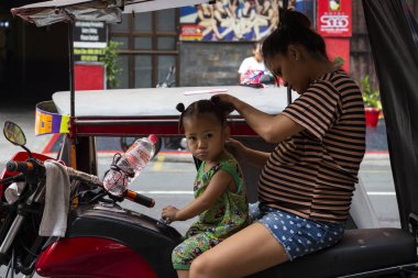 Manila, Filipinler - 14 Nisan 2018: üç tekerlekli bisiklet üzerinde oturan küçük kızına saç yapma anne. Zavallı filippino aile sabah rutin. Filipinli çocuk ile anne motosiklet üzerinde. Asya seyahat sahne