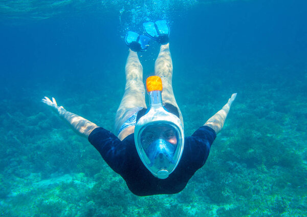 Young woman diving underwater photo. Snorkel in coral reef of tropical sea. Young girl in full-face snorkeling mask. Underwater photo of oceanic landscape. Active seaside vacation. Seaside activity