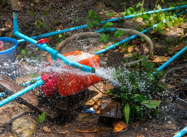 Breakthrough water pipe. Broken water supply. Fresh water recourse waste. South Asia water supply problem. Blue pipes and orange tank mechanism. Splash from pipeline. Broken plumbing in summer garden