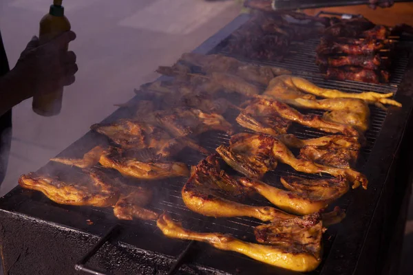 Grilled chicken closeup with cooker silhouette. Street food photo. Hot grill chicken closeup. Cook chief hand with sauce bottle. Cooking grill meat outside. Fried meat barbecue. Poultry roasted