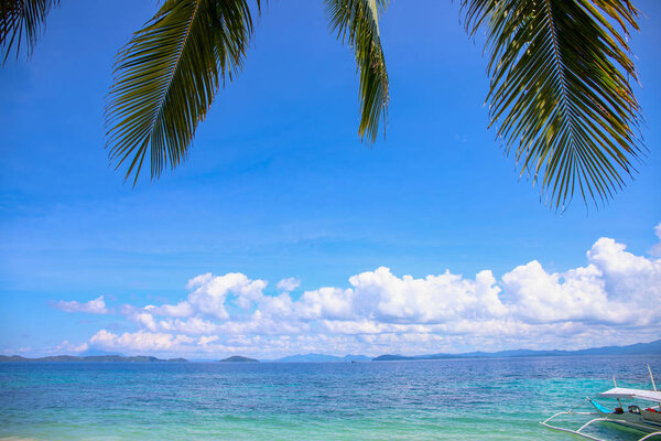 Коко пальмовый лист и голубой морской пейзаж с рыбацкой лодкой. Вид на остров из пальмовых листьев. Экзотический отпуск на морском побережье. Летние каникулы побег назначения. Идиллический шаблон тропического рая
