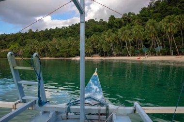 Tropik deniz ve palmiye ağaçları. Tropikal adada tekne turu. Yaz tatili için egzotik bir yer. Filipinler seyahat fotoğrafı. Sarı kumsalda mavi bir tekne. Turistler deniz kenarında dinlenir.