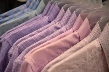 Pastel gömlekler dükkanda satılık. Plastik askıda resmi aşınma. Mağazadaki erkekler için resmi kıyafet. Sıcak hava için ofis kıyafetleri. Alışveriş merkezinde indirim var. Pembe mavi renkli gömlekler.
