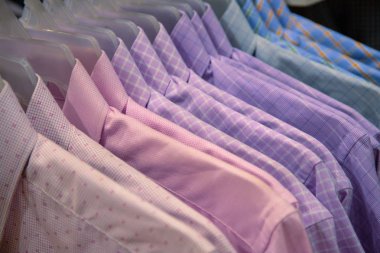 Pastel gömlekler dükkanda satılık. Plastik askıda erkek giysisi. Mağazadaki erkekler için resmi kıyafet. Sıcak hava için ofis kıyafetleri. Alışveriş merkezinde indirim var. Pembe mavi desenli gömlekler