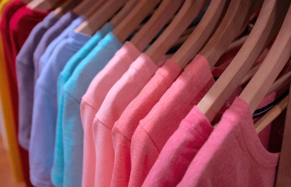Pastel T-shirts on hangs for sale in shop. Candy color wear on wooden hanger. Summer seasonal wear in department store. Feminine apparel for warm weather. Sale in shopping mall. Informal shirt selling