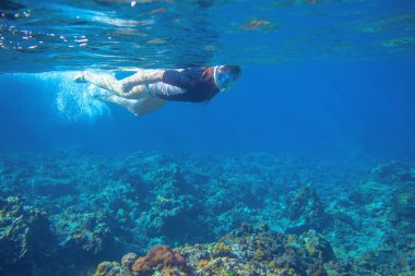Suyun altında şnorkelle yüzen genç bir kadın. Tropikal denizin mercan kayalıklarında şnorkel. Fullface şnorkel maskeli genç kız. Okyanus manzarasının sualtı fotoğrafı. Aktif deniz tatili. Deniz kenarı etkinliği