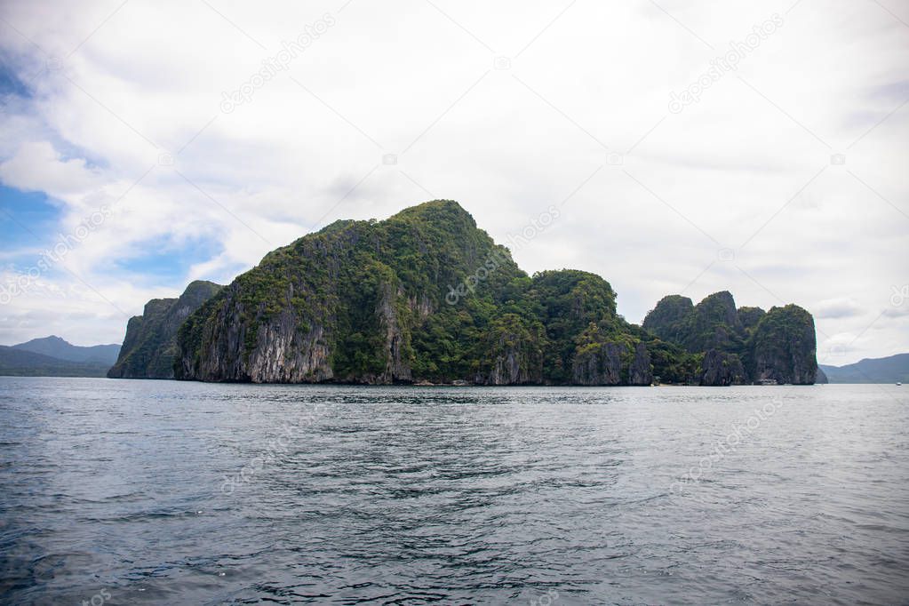 Tropical seaside with still sea water and abandoned island. Black rocks ith green forest in sea. Natural landscape with mountains and sea. Palawan island boat trip. Philippines vacation travel.